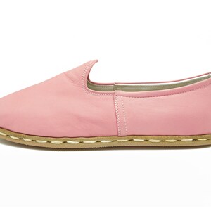 May include: A pair of pink leather slip-on shoes with a brown sole and white stitching.