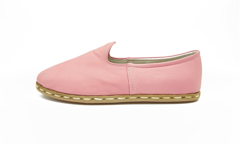 May include: A pair of pink leather slip-on shoes with a brown sole and white stitching.