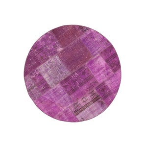 May include: A round, purple patchwork rug with a distressed, vintage look. The rug is made of different pieces of fabric sewn together, creating a unique and eclectic design.