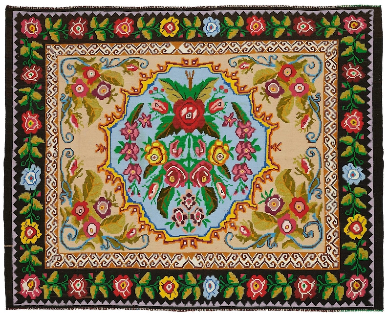 May include: A rectangular rug with a black border and a central design featuring a light blue and beige background. The rug is adorned with a floral pattern in red, pink, yellow, and blue, creating a vibrant and decorative piece.