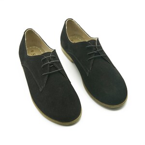 May include: A pair of black suede lace-up shoes with a rounded toe and a brown sole.