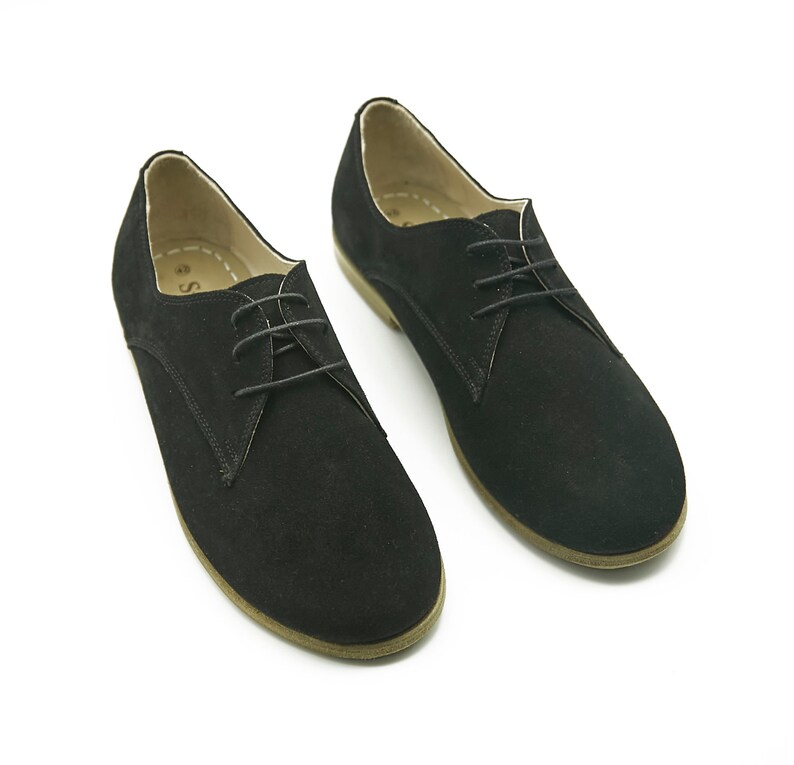 May include: A pair of black suede lace-up shoes with a rounded toe and a brown sole.