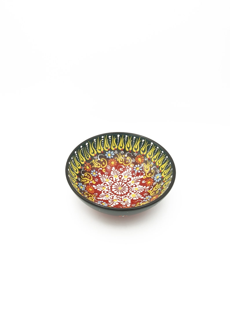 K&ouml;nnte beinhalten: Eine kleine, rote Keramiksch&uuml;ssel mit schwarzem Rand und aufwendigen floralen und geometrischen Mustern in Gelb, Blau und Wei&szlig;.