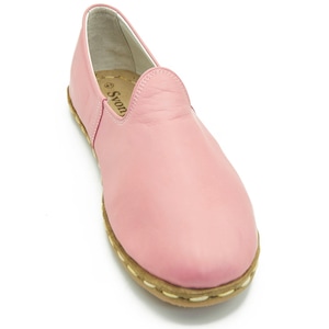 May include: A pair of pink leather slip-on shoes with a white stitched trim around the sole. The shoes have a brand name "Swon" on the inside.