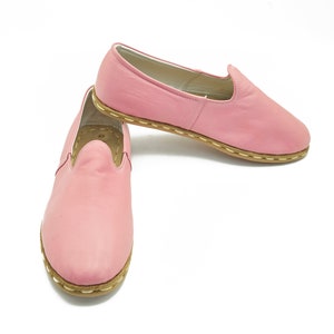 May include: A pair of pink leather slip-on shoes with a brown stitched trim.