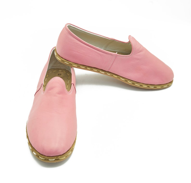 May include: A pair of pink leather slip-on shoes with a brown stitched trim.