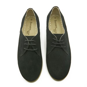 May include: A pair of black suede lace-up shoes with a brown sole. The shoes have a simple design and are made by the brand "Svonny Handmade Shoes".