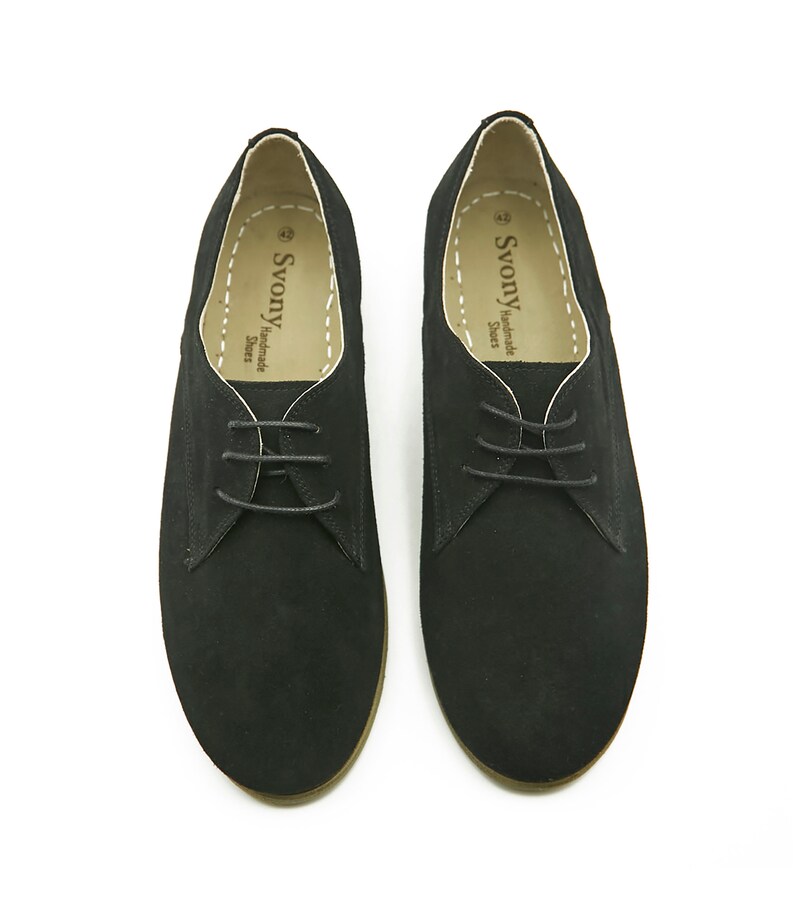 May include: A pair of black suede lace-up shoes with a brown sole. The shoes have a simple design and are made by the brand "Svonny Handmade Shoes".