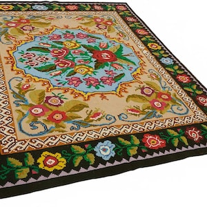 May include: A rectangular, hand-woven rug with a floral design. The rug features a central light blue medallion with a bouquet of red, yellow, and pink flowers. The border is black with colorful floral accents, and the rug measures approximately 60 x 90 inches.