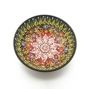 K&ouml;nnte beinhalten: Eine runde Keramiksch&uuml;ssel mit schwarzem Rand und einem farbenfrohen Blumendesign. Die Sch&uuml;ssel ist mit gelben, roten, wei&szlig;en, blauen und gr&uuml;nen Blumen und Spiralen verziert.