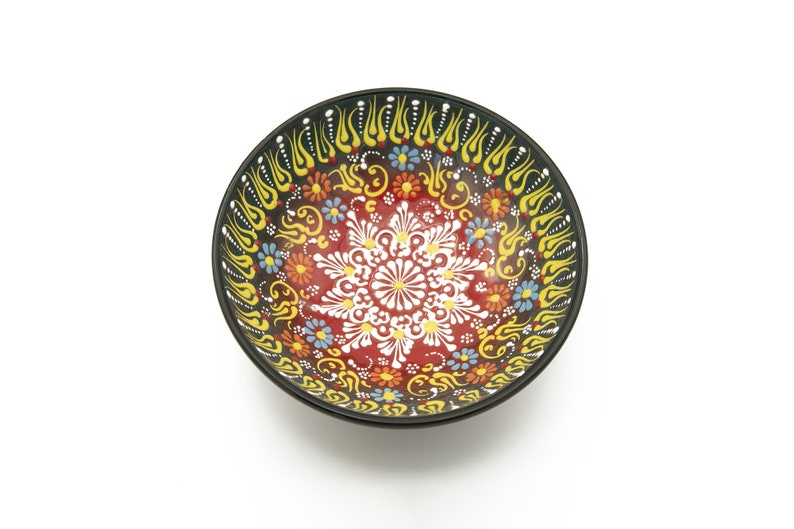 K&ouml;nnte beinhalten: Eine runde Keramiksch&uuml;ssel mit schwarzem Rand und einem farbenfrohen Blumendesign. Die Sch&uuml;ssel ist mit gelben, roten, wei&szlig;en, blauen und gr&uuml;nen Blumen und Spiralen verziert.
