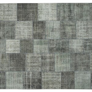 Puede incluir: Una alfombra de patchwork con una variedad de tonos grises y blancos. La alfombra está hecha de diferentes piezas de tela cosidas juntas para crear un diseño único.