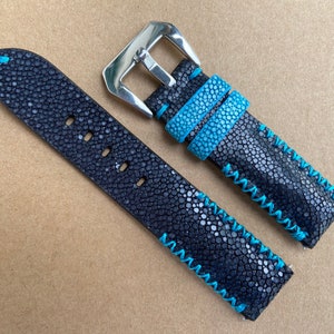 Puede incluir: Correa de reloj de cuero negro con detalles de costura azul. La correa está hecha de piel de raya y tiene una hebilla plateada.