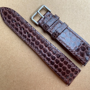 Op de afbeelding: Twee bruine leren horlogebandjes met een krokodillenpatroon. De bandjes zijn gemaakt van echt leer en hebben een zilveren gesp.
