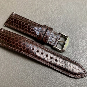 Puede incluir: Una correa de reloj de cuero marrón con un patrón de panal. La correa tiene una hebilla plateada.