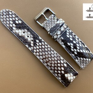 Puede incluir: Una correa de reloj de piel de serpiente marrón y blanca con herrajes plateados. La correa está hecha de cuero genuino y tiene una superficie texturizada.