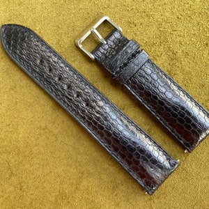 Può includere: Due cinturini per orologio in pelle nera con motivo coccodrilo. I cinturini hanno fibbie argentate.