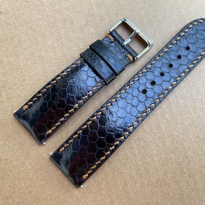 May include: Black leather watch strap with a textured pattern and orange stitching. The strap has a silver buckle.