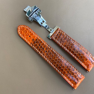 Könnte beinhalten: Ein braunes Lederarmband mit weißen Nähten und einer silbernen Schließe.