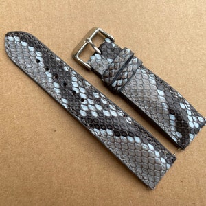 Puede incluir: Dos correas de reloj de piel de serpiente gris y blanca con hebillas plateadas.