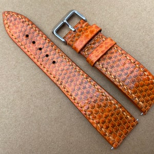 Puede incluir: Dos correas de reloj de cuero naranja con un patrón texturizado y costuras blancas. Las correas tienen hebillas plateadas.