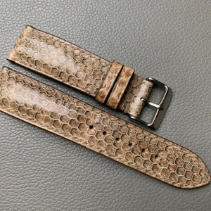 May include: A brown leather watch strap with a honeycomb pattern. The strap has a silver buckle.
