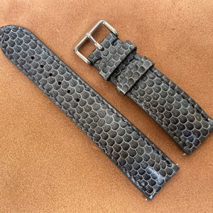 Może przedstawiać: Dwa szare skórzane paski do zegarka z fakturowanym wzorem. Paski wykonane są z miękkiej, elastycznej skóry i mają klasyczny design.