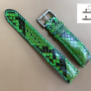 Puede incluir: Una correa de reloj de piel de serpiente verde y negra con herrajes plateados. La correa está hecha de cuero genuino y tiene un borde cosido.