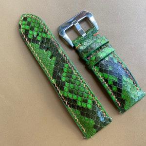 Może przedstawiać: Dwa zielono-czarne skórzane paski do zegarka ze skórą węża z pomarańczowymi szwami. Paski mają srebrne klamry.