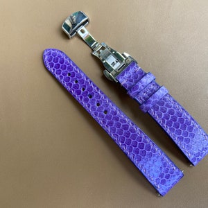 Może przedstawiać: Para fioletowych pasków do zegarka z wzorem skóry gada. Paski są wykonane ze skóry i mają białe szwy. Srebrna klamra jest przymocowana do jednego końca pasków.