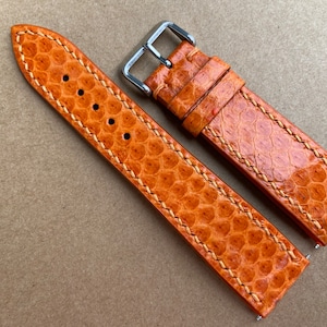 May include: Two orange leather watch straps with white stitching. The straps are made of a textured material that resembles snake skin. One strap has a silver buckle.