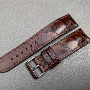 May include: A brown leather watch strap with a unique textured pattern. The strap has a silver buckle.