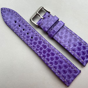 May include: A purple leather watch strap with a textured pattern and white stitching. The strap has a silver buckle.