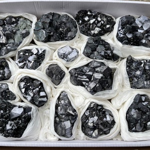 May include: A box filled with small white bags containing black crystals. The crystals are arranged in a variety of shapes and sizes.