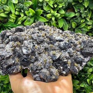 May include: A large mineral specimen featuring a cluster of dark, metallic, angular crystals interspersed with small, shimmering gold-colored pyrite cubes and clear, translucent quartz points across a rugged, textured surface.