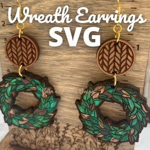 May include: A pair of wooden earrings with a wreath design. The wreath is green with brown leaves and the earrings have a brown and white knit pattern at the top. The earrings are on a wooden background with the text "Wreath Earrings SVG" above them.