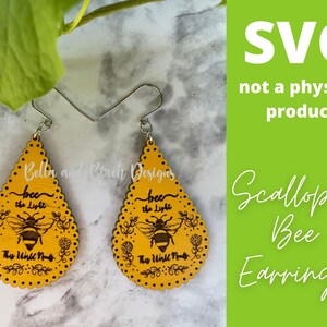 May include: A pair of yellow wooden earrings with a scalloped edge. The earrings are shaped like teardrops and feature a bee with the text "bee the light" and "This world needs" on each earring.
