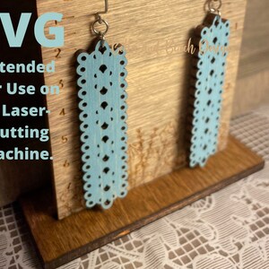 May include: A pair of light blue laser cut earrings with a delicate lace pattern. The earrings are displayed on a wooden stand with a ruler. SVG Intended for Use on a Laser-Cutting Machine.