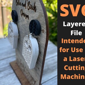 May include: A pair of white layered ghost-shaped earrings on a wooden display stand. The earrings are intended for use with a laser cutting machine. The text "SVG Layered File Intended for Use on a Laser-Cutting Machine." is displayed on a black background.