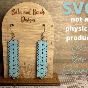 May include: A digital download SVG file for a pair of blue lace bar earrings. The earrings are shown on a wooden display stand with a ruler for size reference. The text "SVG not a physical product Lace Bar Earrings" is also visible in the image.