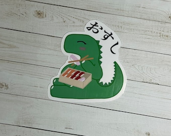 May include: A green dinosaur cartoon sticker with a white background. The dinosaur is holding chopsticks and eating sushi. The text "お ま し" is written in Japanese on the sticker.