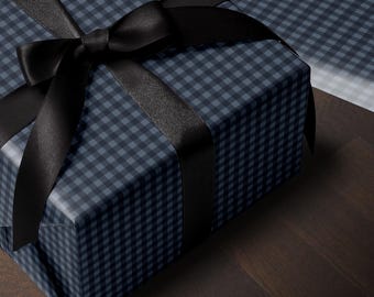 May include: A rectangular gift box wrapped in dark blue and black gingham patterned paper. The box is tied with a wide, smooth black satin ribbon that is knotted into a large bow on the top surface, creating a clean and structured presentation.