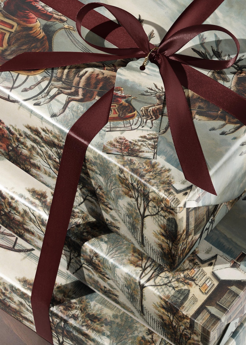 May include: A stack of three rectangular gift boxes wrapped in paper featuring a vintage winter scene with a horse-drawn sleigh and snowy houses. The boxes are tied with a dark burgundy satin ribbon and include a matching gift tag.