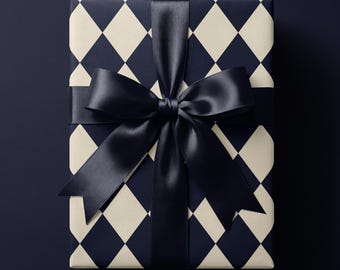 May include: A rectangular gift box wrapped in paper featuring a dark navy blue and cream-colored diamond argyle pattern. The package is tied with a wide, smooth, dark navy blue satin ribbon that is knotted into a large, centered bow on top.