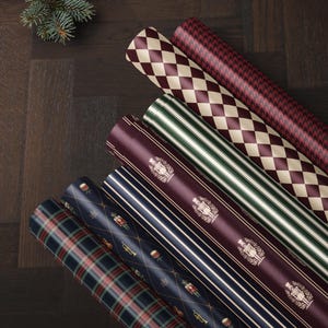 May include: Six rolls of wrapping paper featuring various patterns including a red and cream diamond print, a red houndstooth, green and white stripes, a deep red with gold nutcracker motifs, navy blue stripes, and a navy blue plaid pattern.