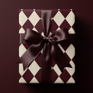 Op de afbeelding: Een rechthoekige geschenkdoos verpakt in papier met een donkerbordeaux en crèmekleurig ruitpatroon. Het pakket is gestrikt met een breed, glad, donkerbordeaux satijnen lint dat is geknoopt tot een grote, centraal geplaatste decoratieve strik.