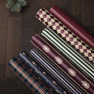 May include: Six rolls of wrapping paper featuring various patterns including a red and cream diamond print, a red houndstooth, green and white stripes, a deep red with gold nutcracker motifs, navy blue stripes, and a navy blue plaid pattern.