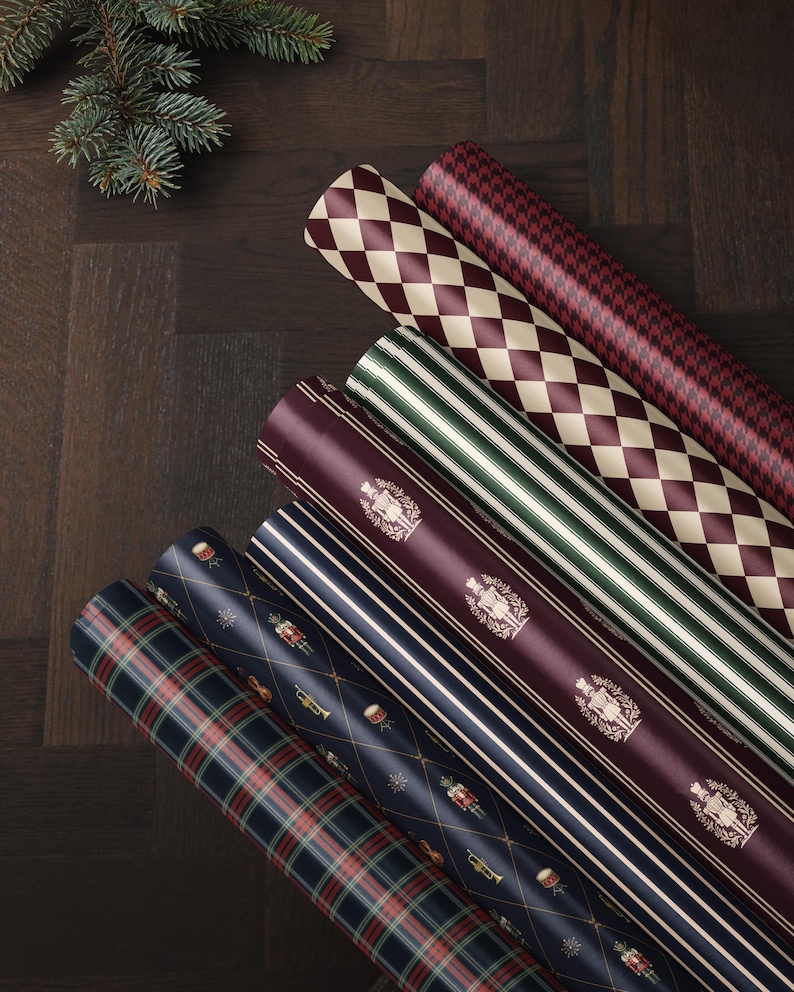 May include: Six rolls of wrapping paper featuring various patterns including a red and cream diamond print, a red houndstooth, green and white stripes, a deep red with gold nutcracker motifs, navy blue stripes, and a navy blue plaid pattern.