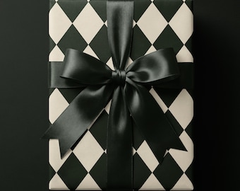 May include: A rectangular gift box wrapped in paper featuring a black and white diamond harlequin pattern. The package is tied with a wide, smooth black satin ribbon that is tied into a large, centered bow with two long, pointed tails.