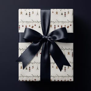 May include: A rectangular gift box wrapped in off-white paper featuring a repeating pattern of small holiday icons including nutcrackers, gingerbread men, stockings, and ornaments hanging from thin green garlands, tied with a wide black satin ribbon.